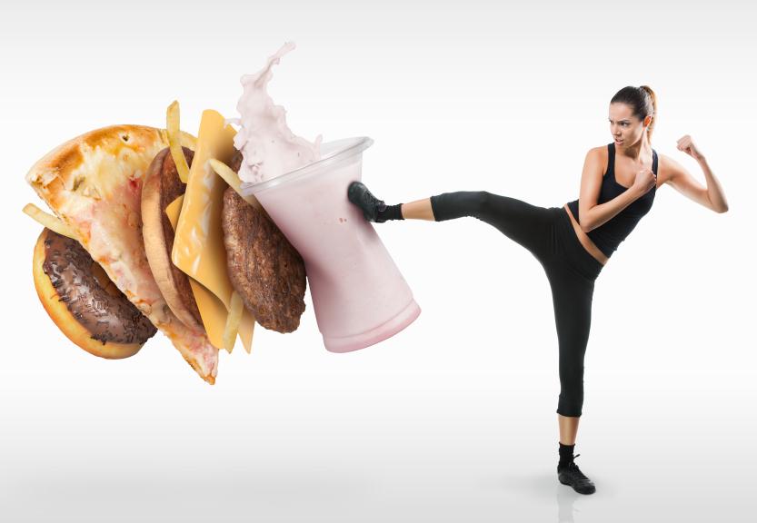 A fit woman kicking unhealthy fast food away.