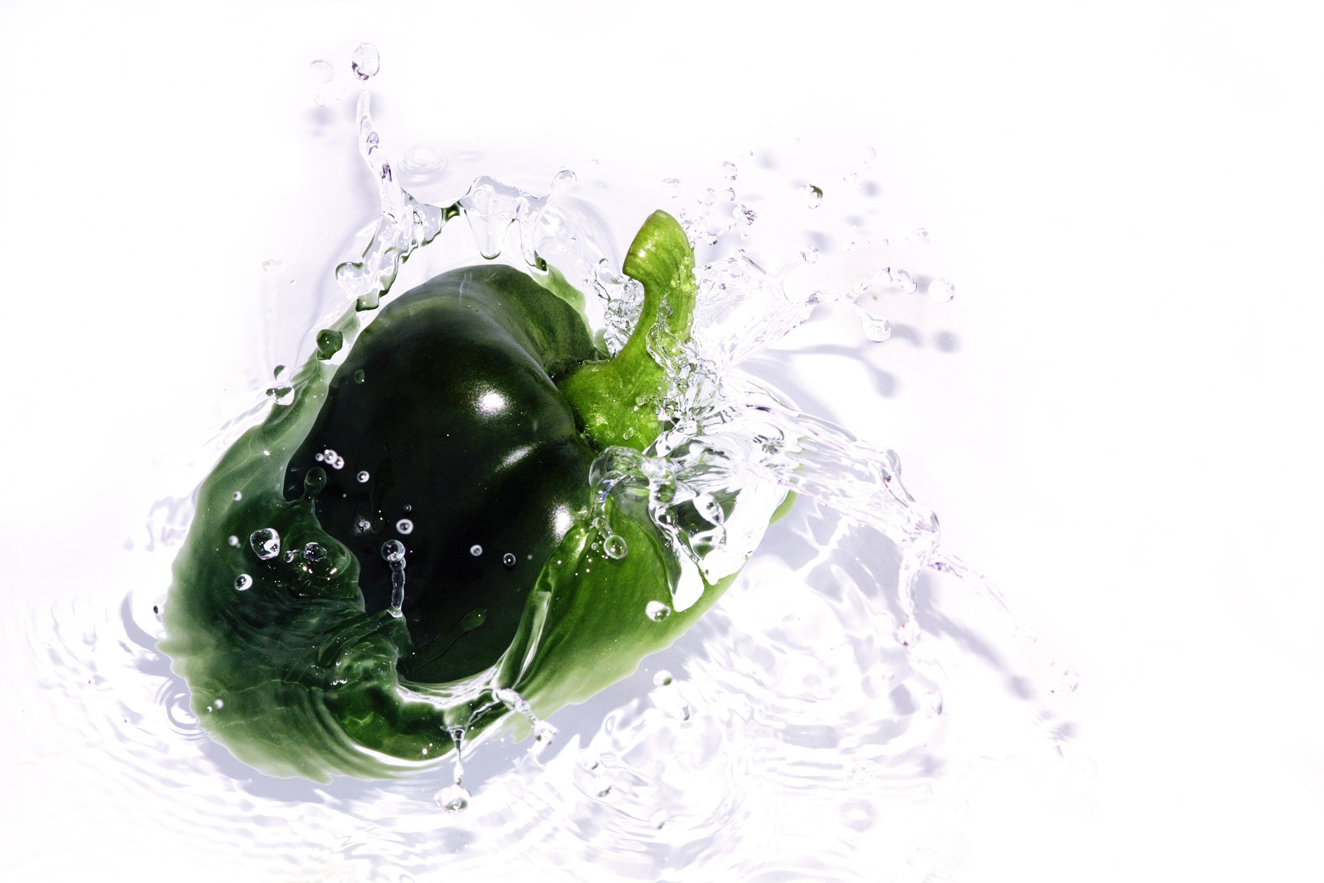 Green bell pepper splashing into clear water on a white background