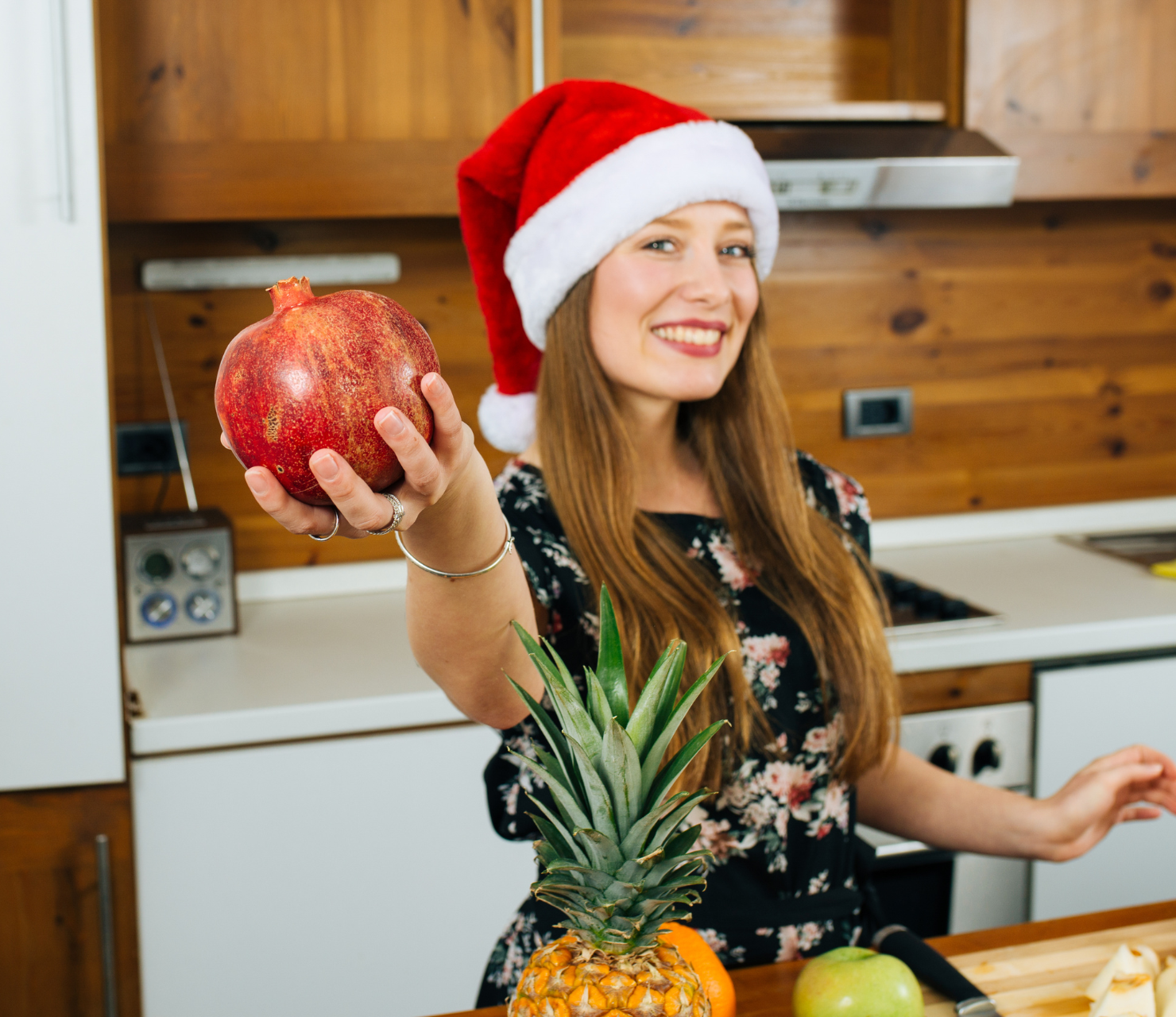 Smiling woman in a Santa hat holding a pomegranate.