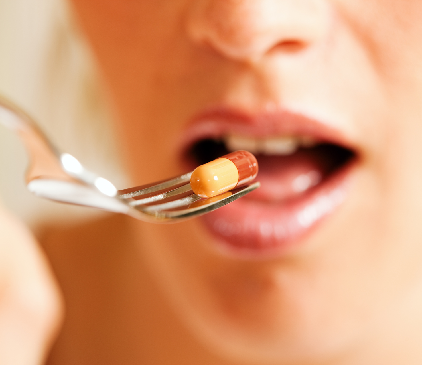 Close-up of a woman taking a capsule with a fork.