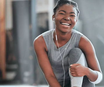 Happy woman in workout clothes smiling with earphones in gym